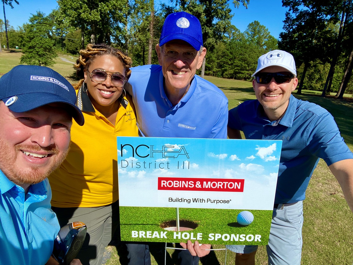 golfers posing by a sign for a tournament