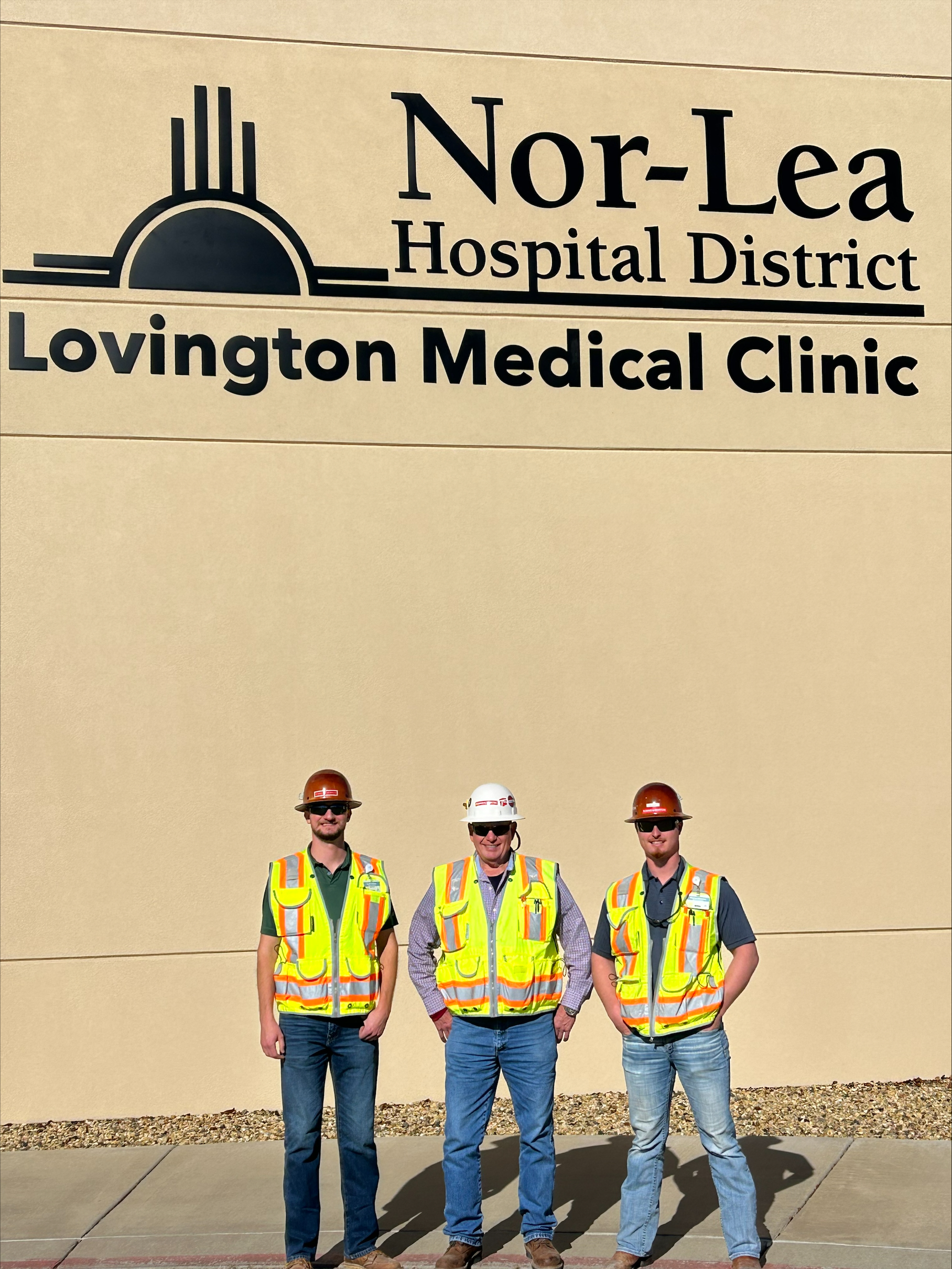 three construction workers standing in front of a hospital