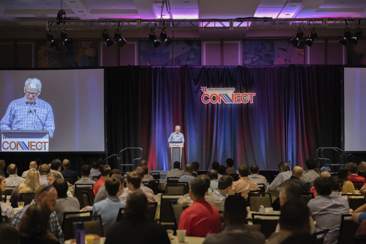 a conference hall with a speaker speaking to a crowd